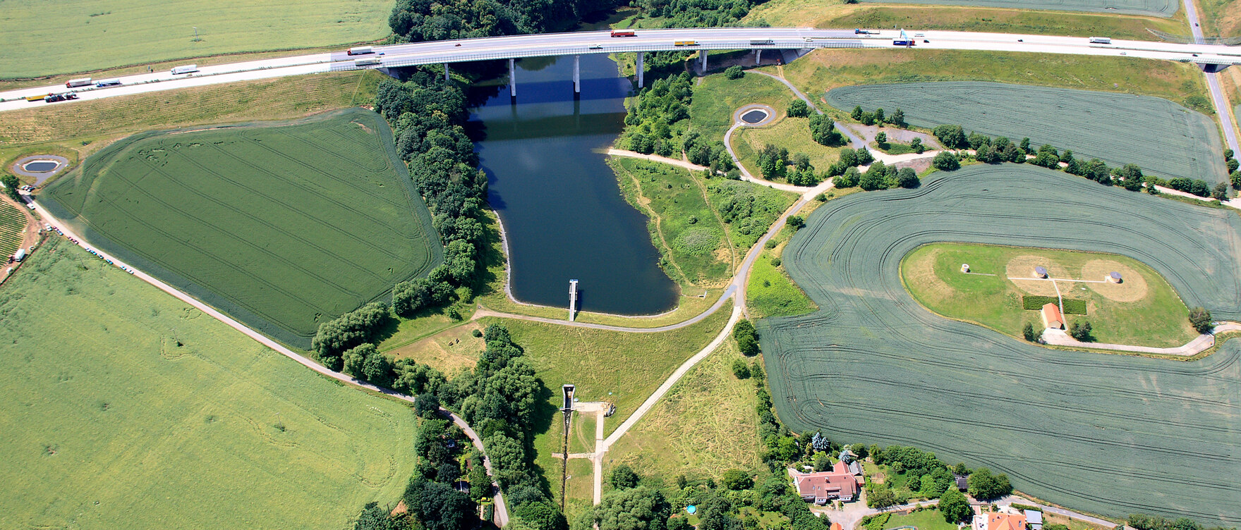 Luftbild einer Talsperre über die eine Autobahn führt, umgeben von Feldern