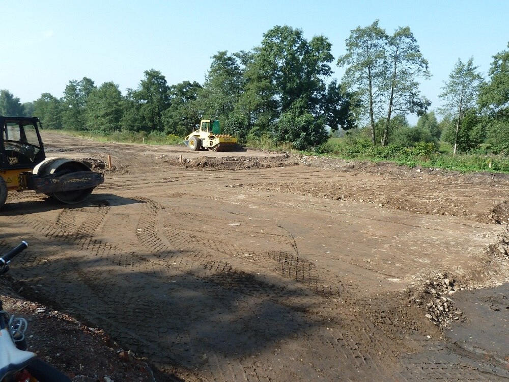 Baustelle mit zwei Baufahrzeugen, im Hintergrund blauer Himmel und grüne Bäume