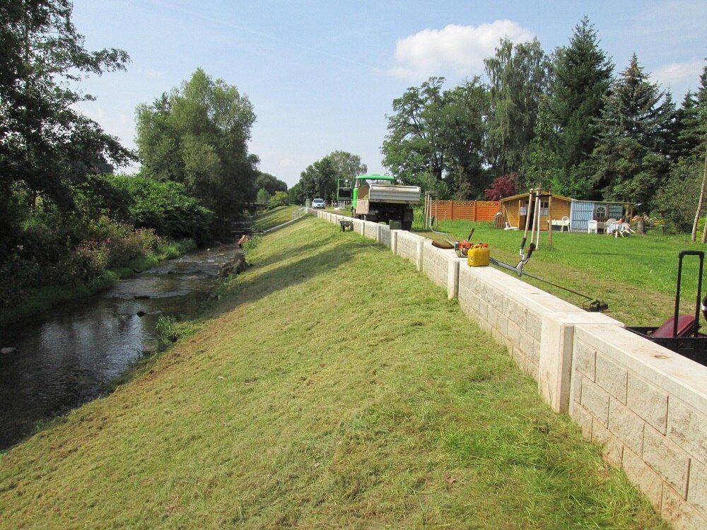 Fluss, flachabfallende Wiese und niedrige Mauer