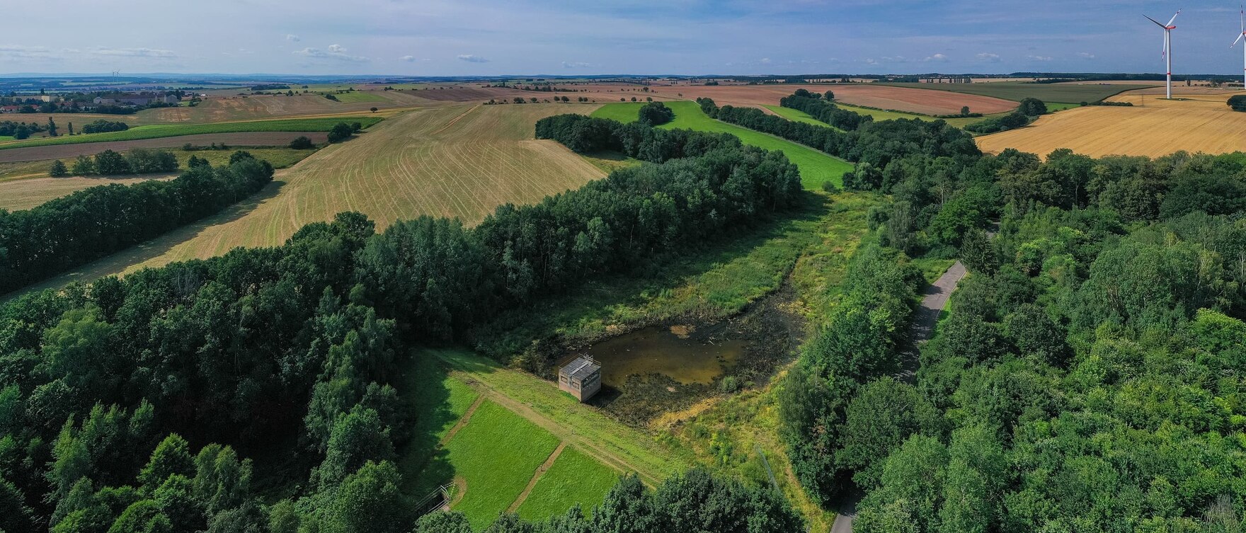 Luftbild der Talsperre Crimmitschau umgeben von Wald und Feldern vor blauem Himmel