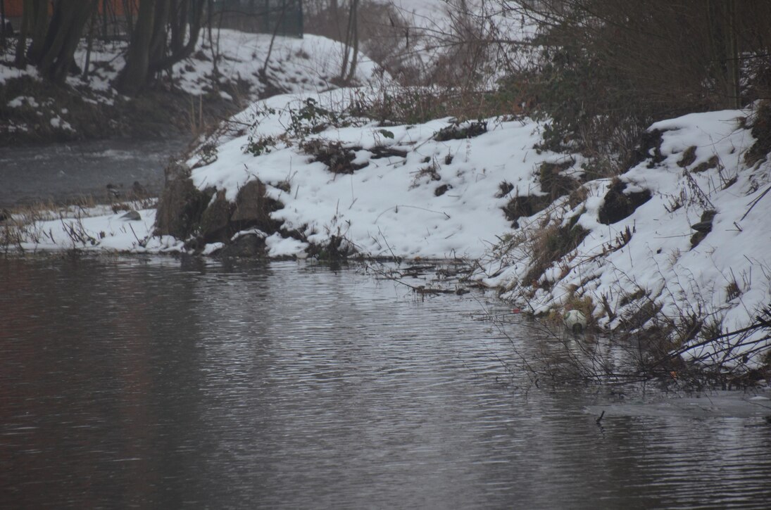 Blick auf Fluss mit Uferböschung, die bedeckt ist von Schnee